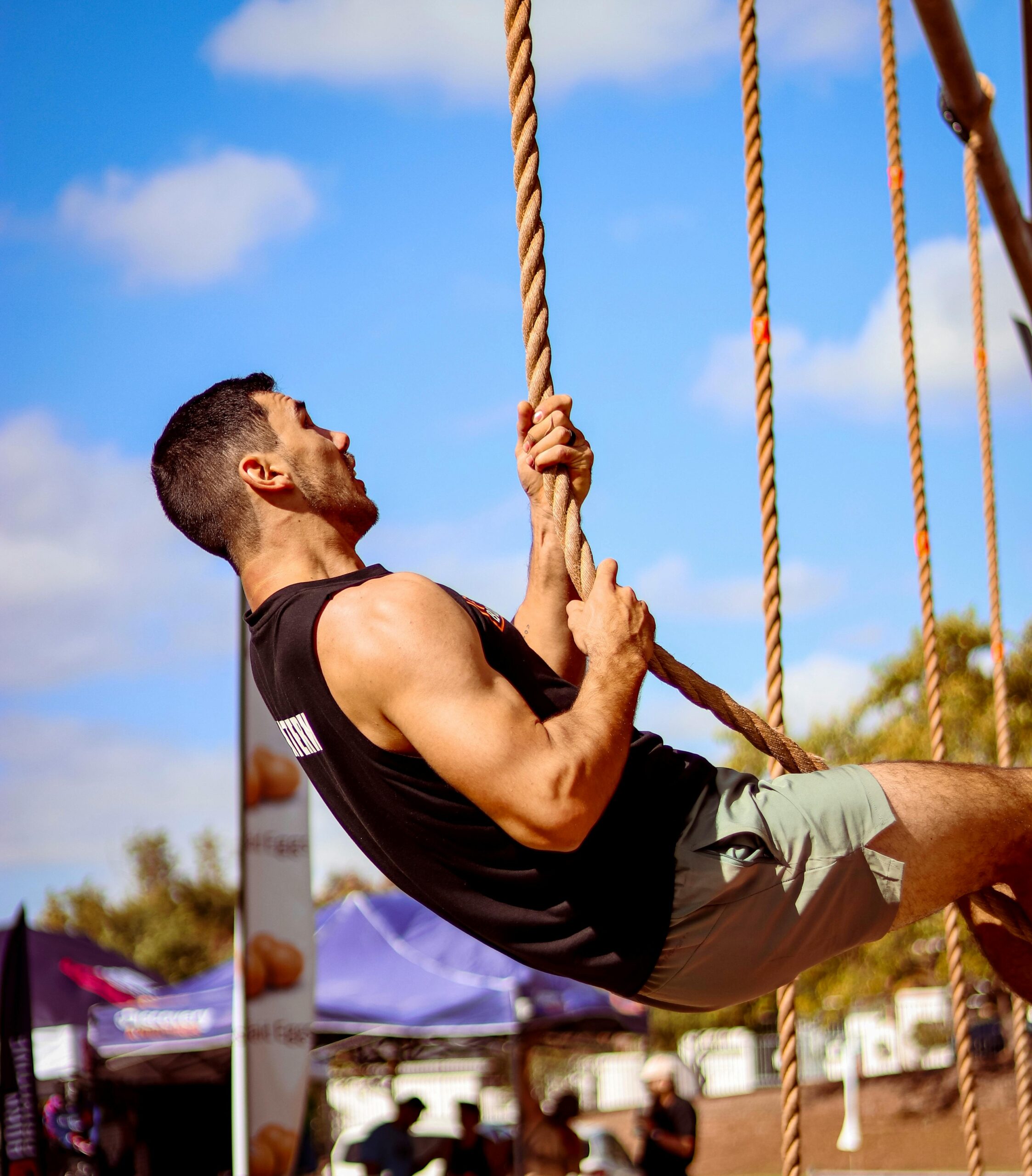 Man climbing rope outdoors during fitness competition showcasing strength and determination.