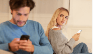 Couple sitting apart and looking at their phones while experiencing relationship distrust