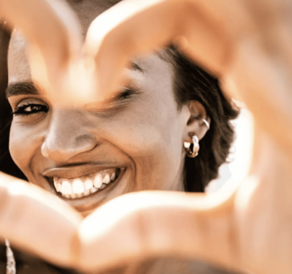 Smiling woman framing her face with her hands in warm, natural light.