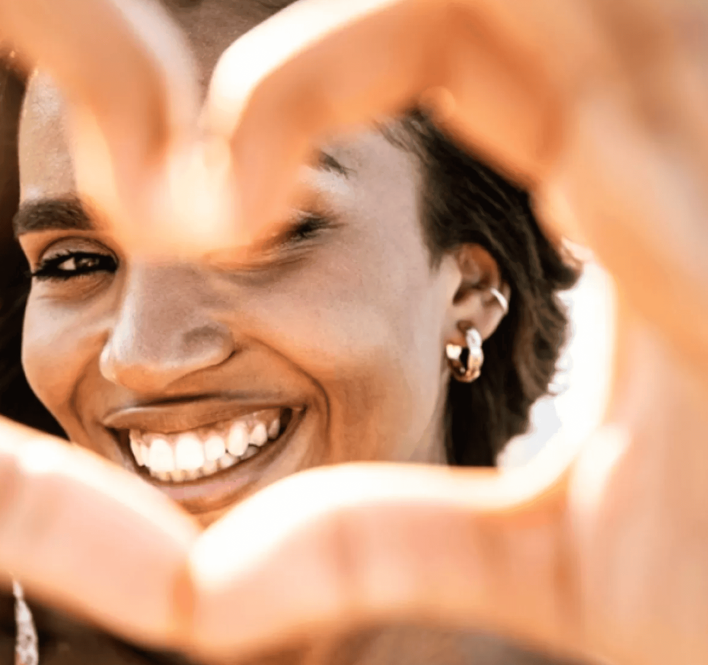 Smiling woman framing her face with her hands in warm, natural light.